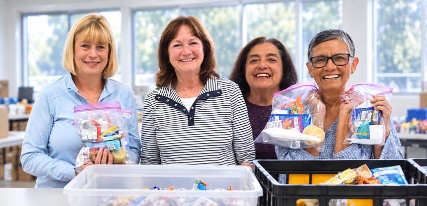 Four smiling women volunteers holding snack packs for those experiencing homelessness